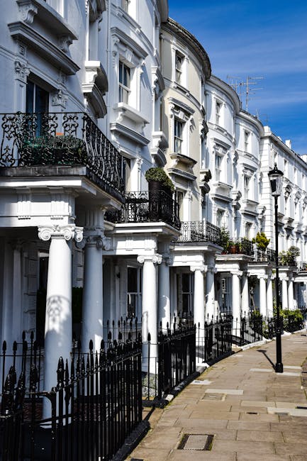 Photograph of a row of white Victorian-style residential buildings with ornate architectural details, including rounded bay windows and decorative columns at the entrance. A leafless tree stands in th