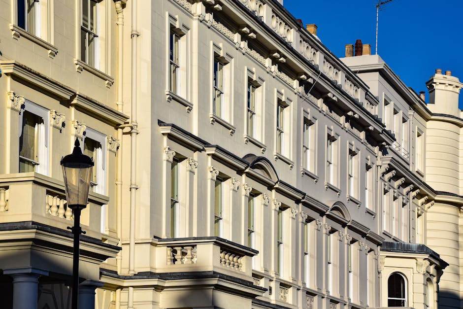 Close-up view of a light beige Victorian-style building façade with decorative molding and multiple rectangular windows, some with iron balconies, under clear blue sky. A black lamppost is positioned in the foreground, emphasizing the building's exterior. The surface appears clean and well-maintained, reflecting natural sunlight, highlighting the architectural details, with no visible dust or dirt. This image illustrates the exterior of Pimlico flats, capturing their ornate detailing and residential character, suitable for content on surface cleaning and property maintenance by Cleaners Pimlico for the SW1V End-of-Tenancy Cleaning Checklist.